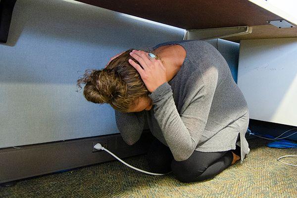 Woman crouching under a desk holding her head, possibly for protection or during an emergency drill.