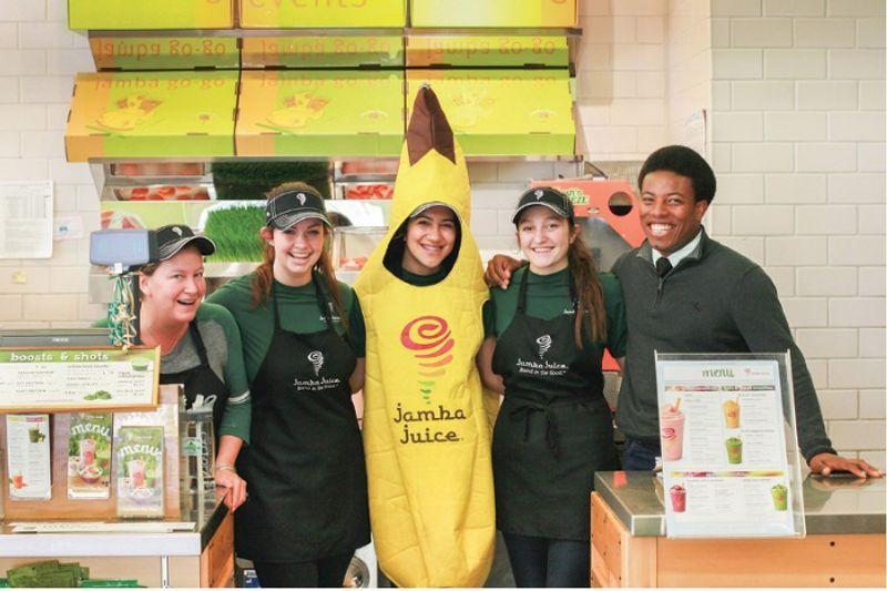 Five Jamba Juice employees smiling, one dressed in a banana costume, standing behind the counter.