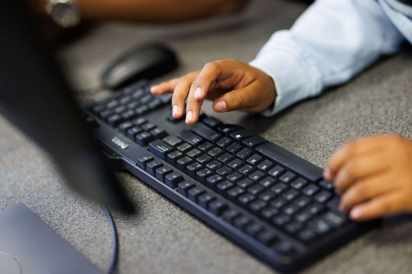 Hands typing on a black Dell keyboard on a gray desk with a computer mouse nearby.