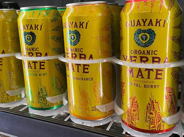 Yellow cans of Guayaki organic yerba mate in flavors: Enlighten Mint, Exuberance, and Revel Berry.