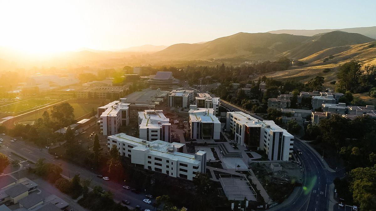 Sunset view of a modern university campus with multiple white buildings and surrounding hills in the background.