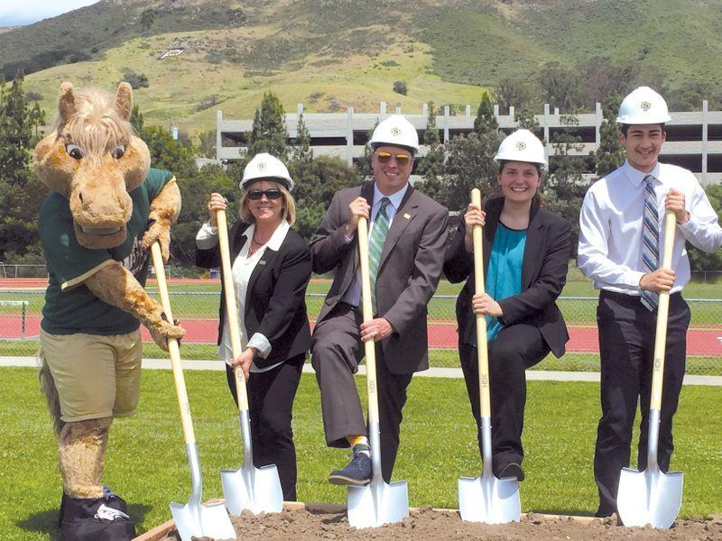 Five people, including a mascot in a horse costume, wearing hard hats, holding shovels, at a groundbreaking event.