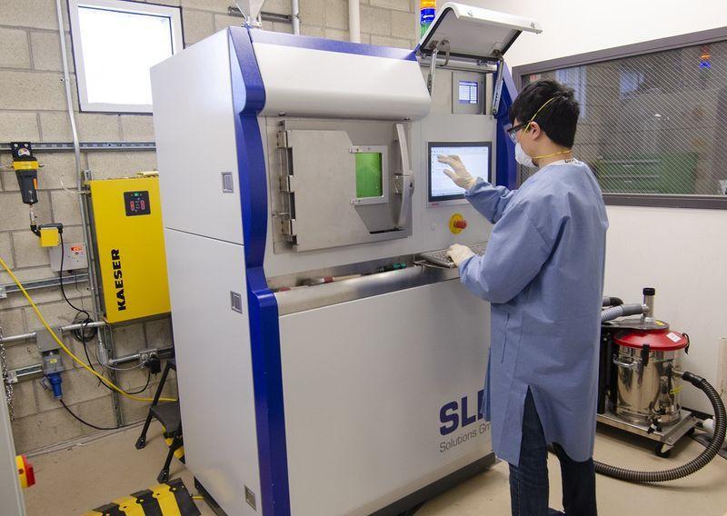 Person in protective clothing operating a large SLA 3D printer in an industrial setting.