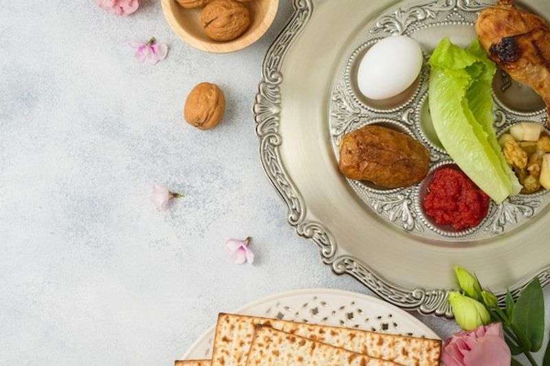 Silver Passover Seder plate with egg, lettuce, charoset, walnuts, and potato, matzah crackers below.