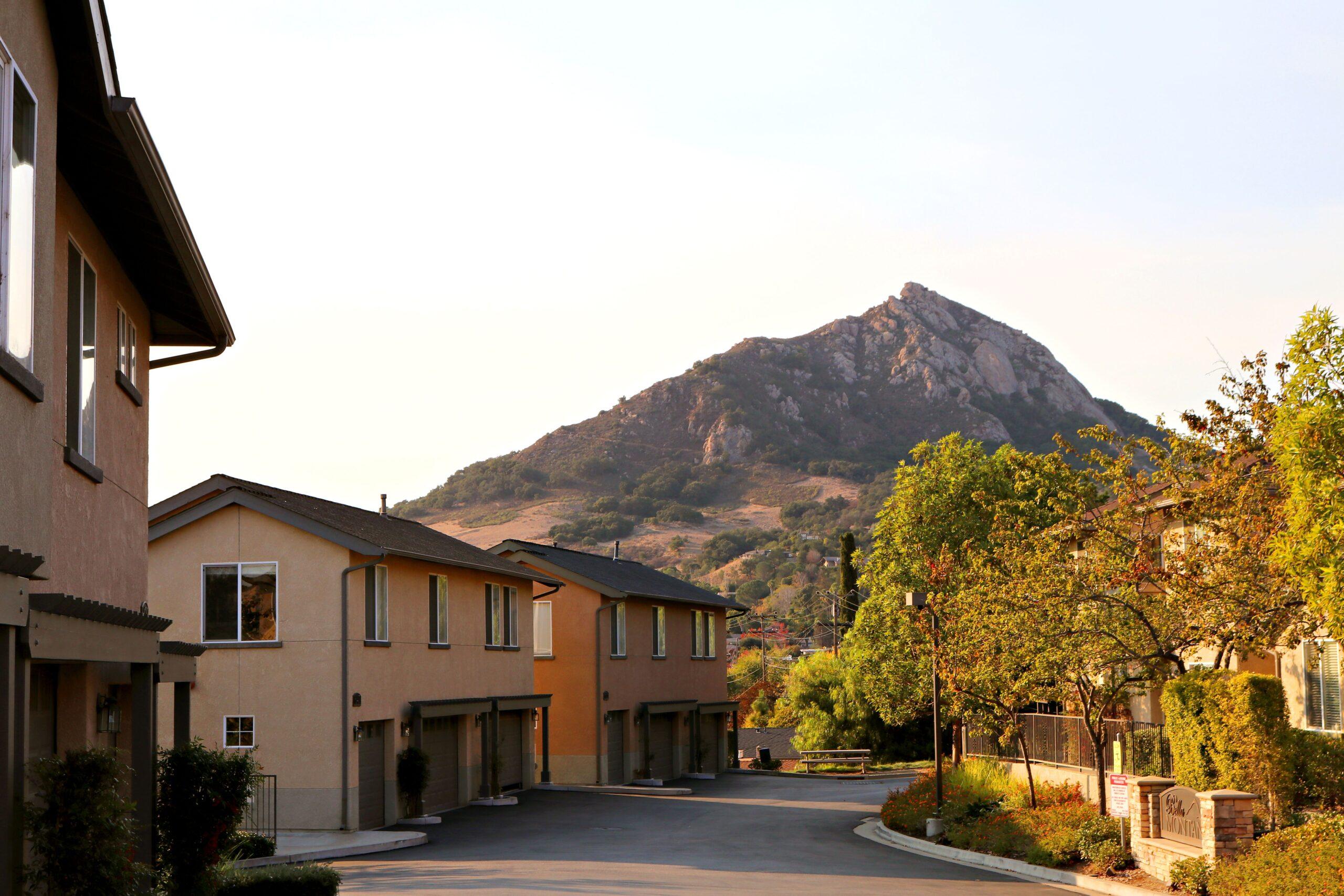 Townhouses along a paved street with a rocky hill in the background and trees on the right side.