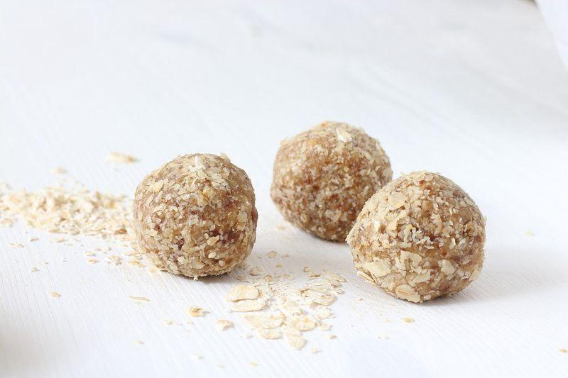 Three energy balls covered in oats on a white surface with scattered oat flakes.