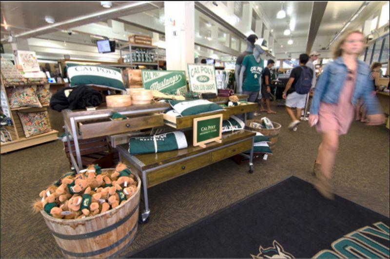 Cal Poly merchandise display with plush toys, pillows, and apparel in a busy college store.