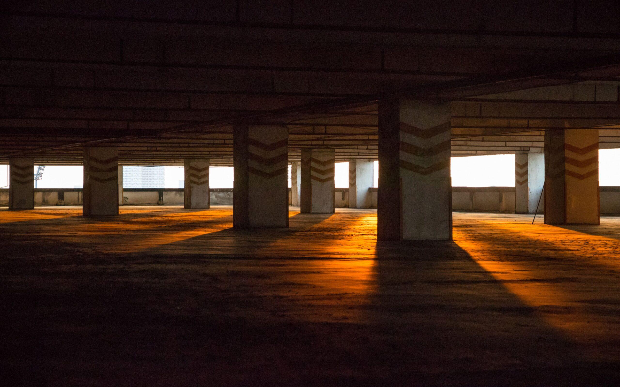 Empty parking garage with concrete pillars casting long shadows from sunlight outside.