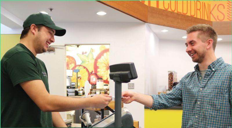 Customer and cashier smiling while exchanging a payment at a counter in a shop.