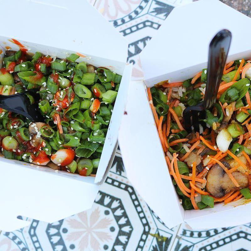 Two takeout boxes with vegetable stir-fry, green onions, carrots, mushrooms, sesame seeds, and dark plastic forks.