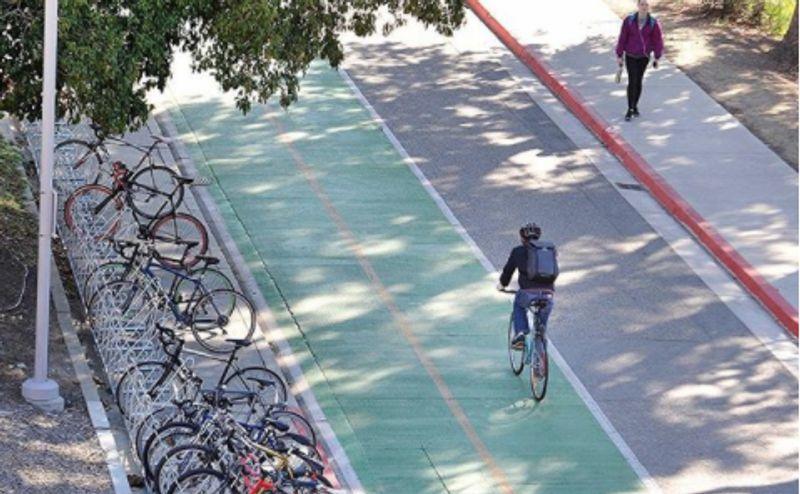 Bicyclist on green bike lane next to parked bicycles and a pedestrian walking on sidewalk.