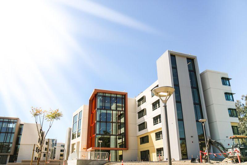 Modern multi-story buildings with large windows under a clear blue sky and bright sunlight.