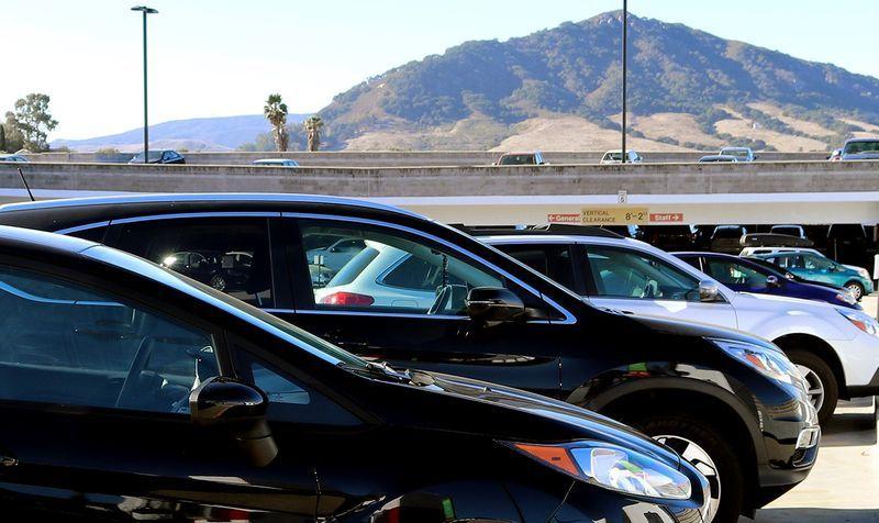 Several parked cars in a parking lot with mountain hills and clear sky in the background.