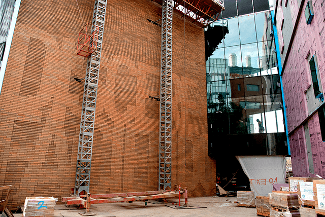 Construction site with brick wall, metal scaffolding, reflective glass building, and building materials.