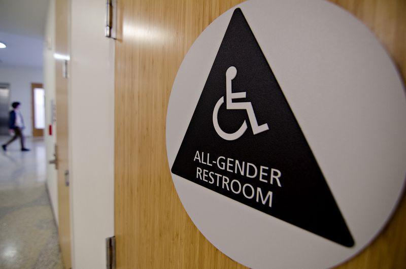 All-gender restroom sign with wheelchair accessibility symbol on a wooden door in a hallway.