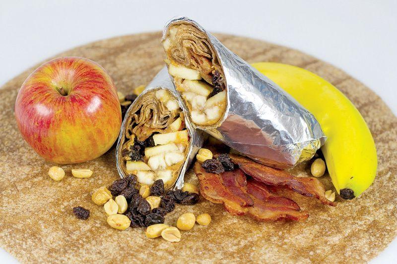 Apple, banana, bacon, raisins, and peanuts with a wrapped and halved peanut butter and banana tortilla.