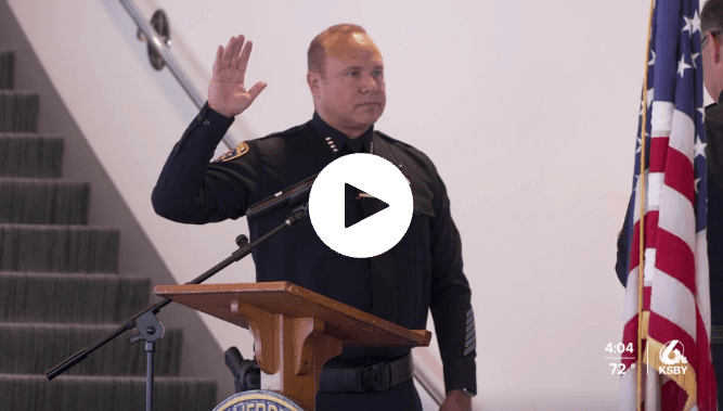Police officer raising right hand, taking an oath in front of an American flag and podium.