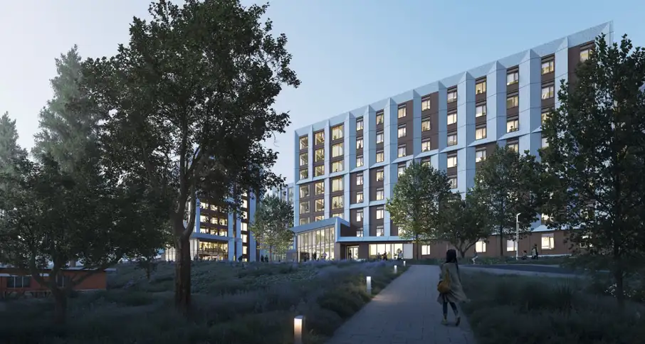 Modern residential buildings with illuminated windows at dusk, surrounded by trees and walking paths.