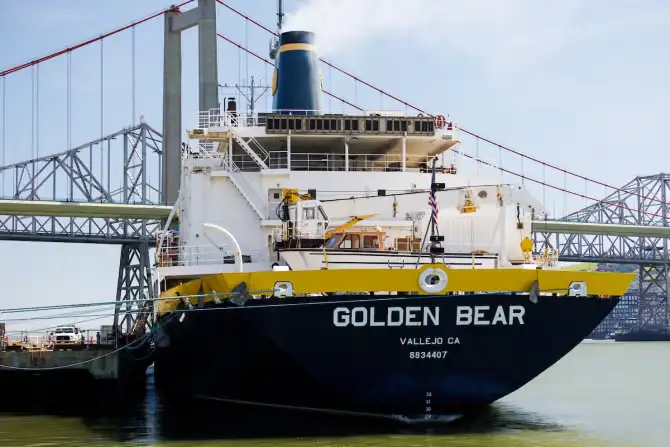 Large ship named GOLDEN BEAR from Vallejo CA docked near several bridges on a sunny day.